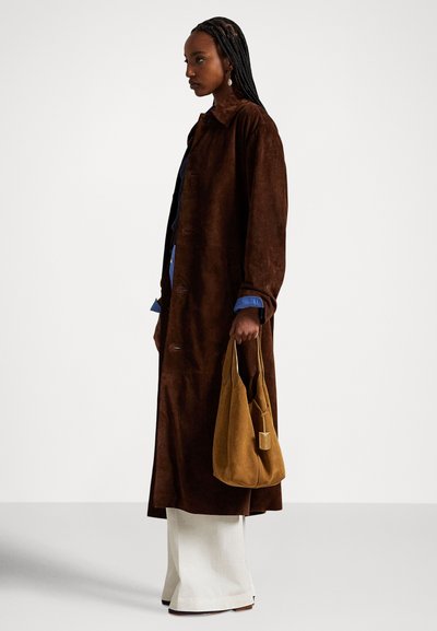 Hnedý semišový kabát s golierom, zapínaním na gombíky a bočnými vreckami. Kombinovaný so svetlomodrou košeľou, širokými krémovými nohavicami a hnedou taškou cez rameno.