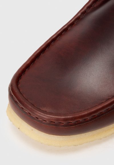 Zapato de cuero marrón con un acabado suave, punta redondeada y suela beige contrastante. El detalle de costura a lo largo del borde añade textura.