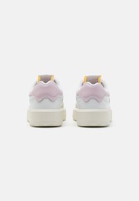 Zapatillas blancas con acentos en rosa y amarillo, que cuentan con un talón texturizado y una suela gruesa en color beige. Diseño redondeado con materiales suaves.
