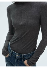 Bodysuit gris à manches longues avec un col montant et une découpe rectangulaire à l'avant, associé à un jean en denim bleu taille haute. Texture lisse, design ajusté.