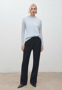 Maglione leggero di colore azzurro, con scollo rotondo, abbinato a pantaloni neri ben sagomati e tacchi a punta neri. Design semplice.