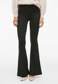 Pantalones de campana negros hechos de un material suave y elástico; cintura alta, ajustados en los muslos, que se ensanchan desde la rodilla. Sin patrones visibles.