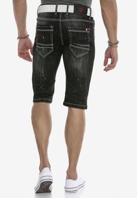 Schwarze Jeansshorts mit slim Fit, ausgestattet mit einem umgeschlagenen Saum, ausgefransten Details und einem weißen Nieten-Gürtel. Zwei sichtbare Gesäßtaschen.