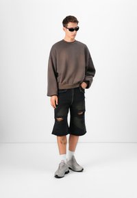 Sweatshirt oversized cinza escuro, calções de ganga pretos desgastados, ténis cinzentos, meias brancas e óculos de sol pretos. Apresenta rasgos e desfiados em destaque.