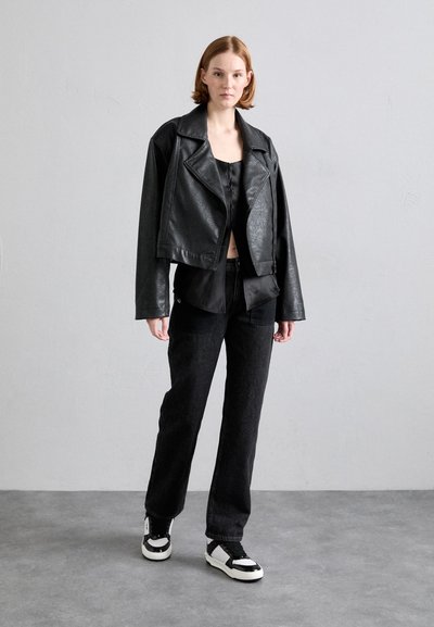 Black faux leather cropped motorcycle jacket over a black shirt, paired with black jeans and black and white sneakers; smooth texture.