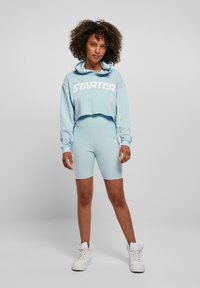 Svetlo modrý cropped hoodie s logom "STARTER", doplnený o zodpovedajúce priliehavé šortky. Biele vysoké tenisky dotvárajú vzhľad. Mäkká textúra.