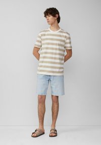 T-shirt beige et blanche à rayures, shorts en denim et sandales marron. Style décontracté avec un col rond et des manches courtes.