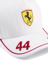 Biała czapka baseballowa o żłobionej teksturze, z czarnym i żółtym logo Ferrari z przodu oraz czerwonym haftem "44" na daszku.