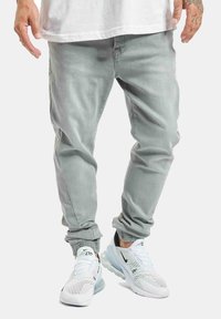 Jeans tapered de color gris claro con puños elásticos y bolsillos, combinados con zapatillas blancas que presentan detalles de malla y amortiguación de aire.