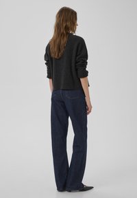 Suéter corto de color gris oscuro con puños acanalados, combinado con jeans de color azul oscuro de corte holgado. Modelo de espaldas sobre un fondo liso y claro.