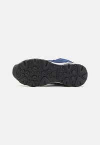 Blå sneakers med en teksturert svart gummisåle som har sirkulære og sikksakkmønstre. Holdbart yttermateriale med kontrasterende aksenter.