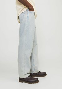 Jeans de mezclilla azul claro con un corte holgado, diseño de cinco bolsillos y pierna recta. Combinados con zapatos marrones de cordones.