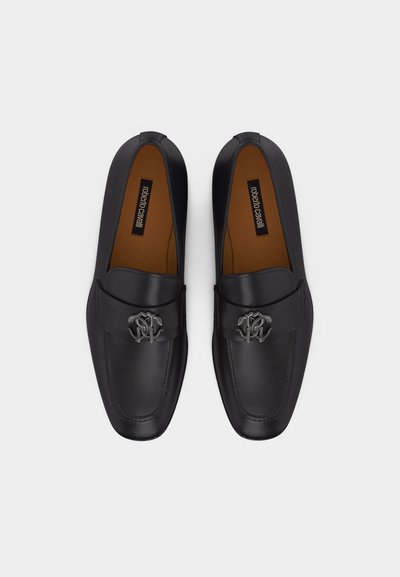 Čierne kožené mokasíny so strieborným dekoratívnym logom na remienku, hnedé stielky označené "roberto cavalli," pohľad zhora na bielom pozadí.