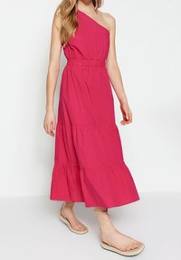 Fuchsiová maxidélka šatů na jedno rameno s přiléhavým pasem a vrstveným volánkovým lemem. Vyrobeno z lehkého materiálu. Nosené s béžovými sandály na řemínky.