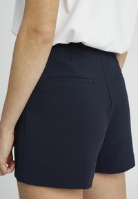 Shorts ajustés bleu marine en tissu lisse, présentant un design épuré, deux poches arrière et un ourlet droit.