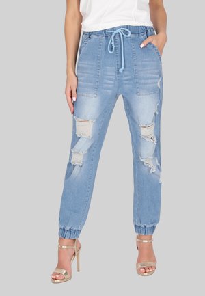 Lichtblauwe denim joggers met versleten scheuren, elastische boorden en een tailleband met trekkoord. Gecombineerd met gouden strappy hakken.