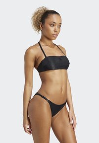 Čierny bikiny s rebrovanou textúrou, s nastaviteľnými ramenami na vrchu a minimálnym zakrytím spodnej časti, zdôrazňujúci priliehavý dizajn.
