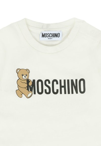 Maglietta bianca per bebè con una grafica di un orsetto che abbraccia la lettera "M" nel testo in grassetto nero "MOSCHINO" sul davanti.