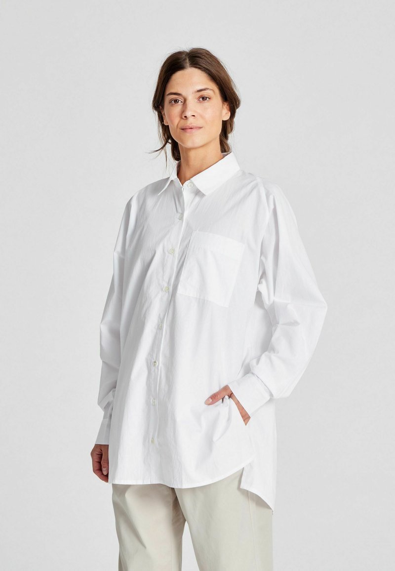 Camicia bianca a maniche lunghe con collo, una tasca sul petto e vestibilità morbida. Realizzata in tessuto leggero con una superficie liscia.