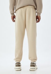 Pantalones de chándal beige con un corte relajado, cinturilla elástica y puños. Hechos de una tela suave, con una textura lisa y sin patrones visibles.