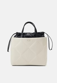 Sac cabas matelassé beige avec poignées en cuir noir et haut à cordon, arborant un petit logo CK au centre avant.