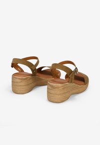 Sandalias de plataforma de ante marrón con correas cruzadas, correa de tobillo ajustable y suela de madera texturizada en diseño estratificado.