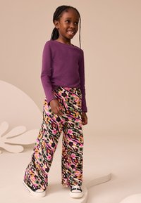 Purple long-sleeve top paired with wide-legged, patterned pants in bright colors including pink, green, and black. Footwear: black and white sneakers.