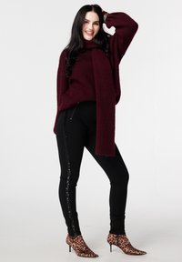 Bordeauxrode gebreide trui met een losse pasvorm, gecombineerd met zwarte legging met pailletten zijstrepen en enkellaarsjes met dierenprint.
