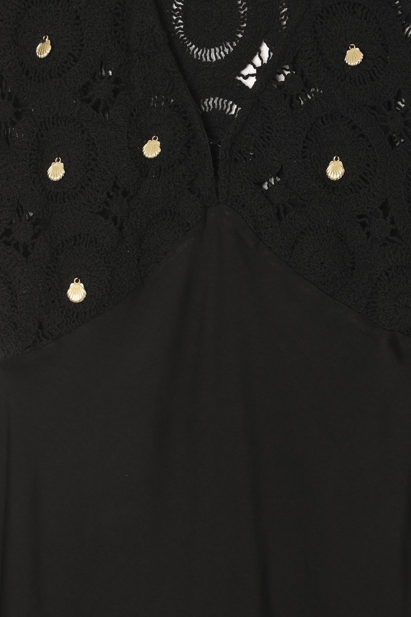 Schwarzes Kleid mit komplizierter schwarzer Spitze am oberen Teil, geschmückt mit goldenen, muschelförmigen Akzenten, das unten in einen glatten schwarzen Stoff übergeht.