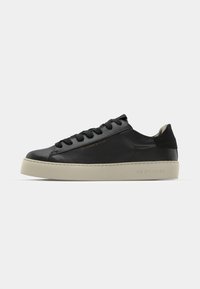 Sneaker in pelle nera con punta rotonda, lacci frontali e suola in gomma spessa color crema. Presenta un dettaglio del marchio in rilievo sul lato.