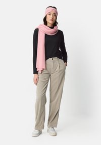 Czarna bluzka z długim rękawem, jasnoróżowy szalik i opaska na głowę. Beżowe, szerokie spodnie o fakturze. Całość uzupełniają białe trampki.