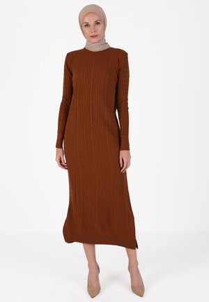 Long brown ribbed dress with long sleeves, high neckline, and side slits. The fabric has a textured pattern. Worn with a beige hijab.