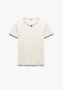 Camisa blanca de manga corta con un patrón vertical texturizado, cuello redondo ribeteado en negro y un pequeño detalle de lazo negro en el escote.