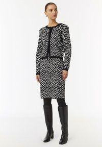 Zwart-wit gestreepte gebreide cardigan over een bijpassende rok, met een ronde hals, lange mouwen en knopen. Draagt een paar zwarte knie-hoge laarzen.