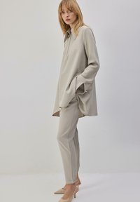 Tunique gris clair avec col et manches longues, associée à un pantalon ajusté assorti. Tissu lisse ; ourlet ouvert.