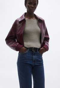 Bordó bőrdzseki galléros nyakkivágással, világosszürke, texturált kötött pulóver fölött viselve, magas derekú kék farmerrel párosítva.