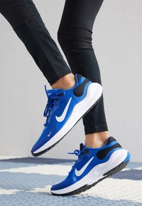 Baskets de sport bleues en mesh et en matériau synthétique, avec un logo Swoosh blanc, des accents noirs et une semelle noire texturée.