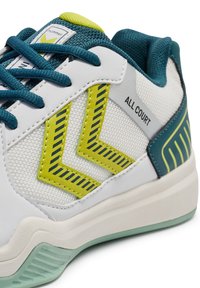 Hvid sportsko med mesh og læder, med turkis snørrebånd, grønne detaljer og et zigzag-mønster. Sål er lysegrå med tekstureret detaljer.