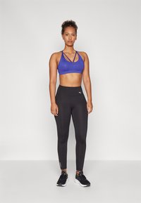 Blauwe sportbeha met kruislings gespen en sprankelende accenten, gecombineerd met hoge zwarte leggings met een logo en ritsen bij de enkels.