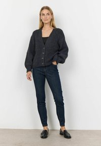 Cardigan lavorato a maglia grigio scuro con scollo a V, sei bottoni e maniche oversize, abbinato a jeans scuri e mocassini neri.