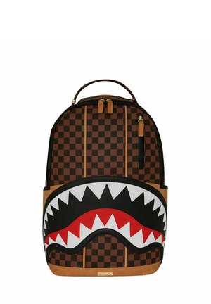 Mochila de lona a cuadros marrón con un diseño de cara de tiburón en blanco y negro, acentos rojos y fondo de cuero sintético marrón. Cuenta con doble cremallera.
