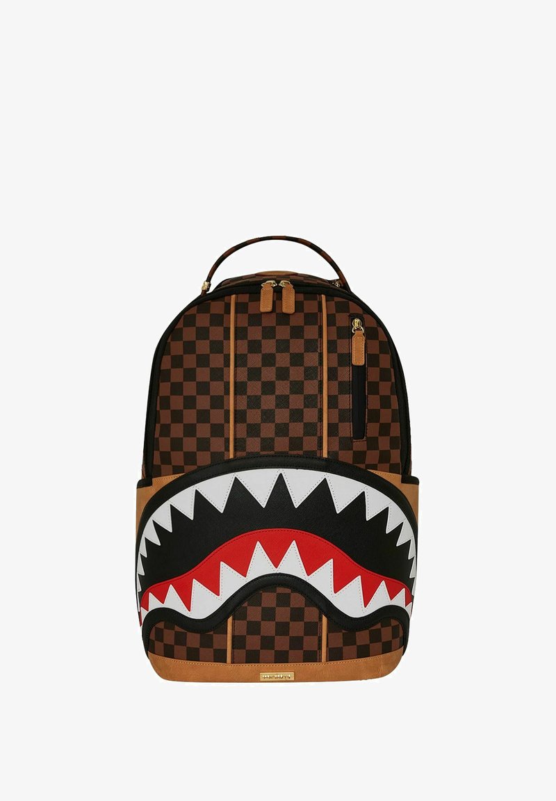 Zaino in tela a quadri marrone con un design di faccia di squalo bianco e nero, dettagli rossi e fondo in pelle sintetica marrone. Presenta due zip.
