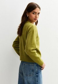 Olijfgroene trui van zachte stof, met een losse pasvorm, verlaagde schouders en geribde manchetten, gecombineerd met blauwe denim jeans.