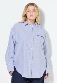 Camicia a righe blu e bianche con bottoni, maniche lunghe, orlo arrotondato e testo ricamato sul petto. Realizzata in tessuto leggero.