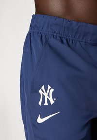 Námornícke športové šortky s elastickým pásom. Obsahujú biele logo NY a biely Nike swoosh na boku. Hladká textúra látky.