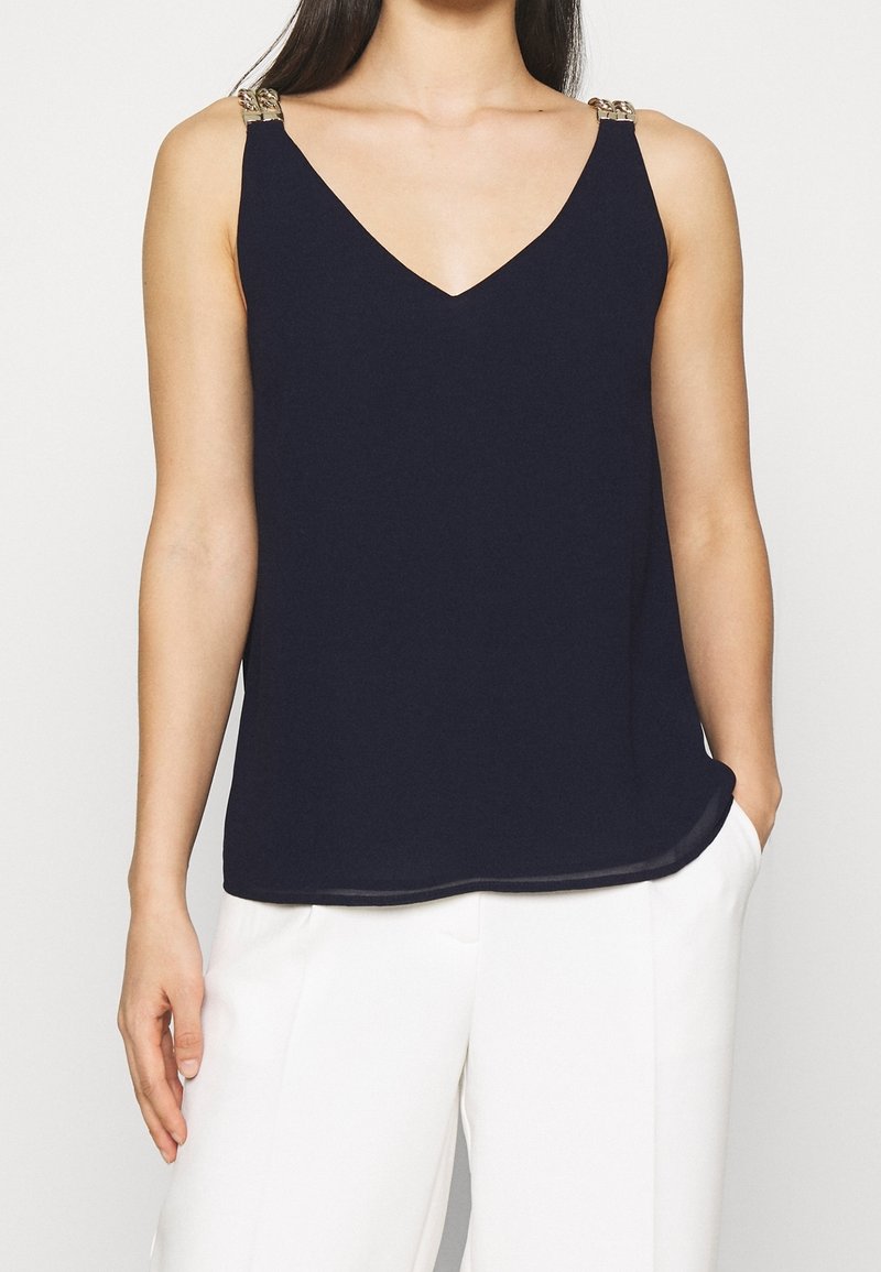 Marinblå linne med V-ringning och metallkedjeprydnader på axelremmarna. Tillverkat av ett mjukt tyg; avkopplad passform.