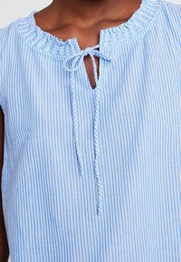 Primo piano di una blusa a righe verticali blu e bianche con scollatura a chiave legata con nastri dello stesso tessuto.