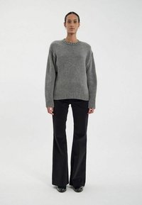 Pull en tricot gris à encolure ronde et ourlet côtelé, associé à un pantalon noir évasé et des chaussures noires. Texture lisse, coupe d écontractée.