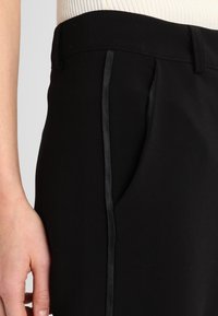 Pantalons noirs ajustés avec une coupe slim, dotés d'une poche latérale élégante et d'une bordure en satin sur le côté pour un contraste de texture.
