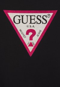 Schwarzes T-Shirt mit einem großen dreieckigen Logo in Weiß und Pink, verziert mit Strasssteinchen, auf dem "GUESS," "WASHED" und ein Fragezeichen zu sehen sind.